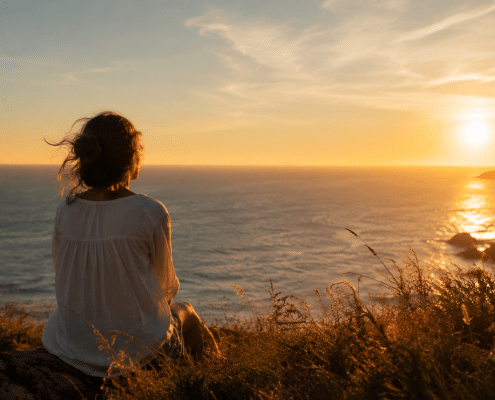 Personne contemplant un paysage d’été au coucher du soleil dans une ambiance douce et introspective